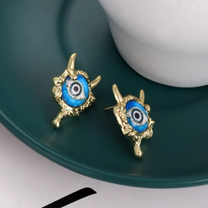 Detailed view of evil eye stud earrings with gold claw design on a ceramic plate