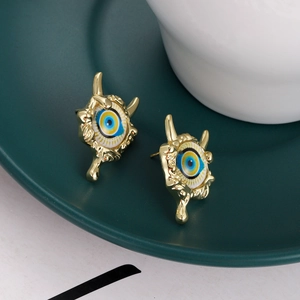Detailed close-up of gold-plated evil eye stud earrings on a dark green ceramic tray