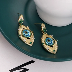 Macro detail of bohemian evil eye earrings with blue enamel and green gems on a tray
