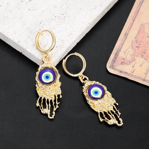 Detailed close-up of golden evil eye earrings with molten texture on dark background