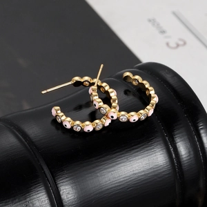 Macro view of gold C-shaped hoop earrings with pink evil eye enamel and crystals