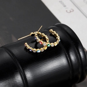 Detailed view of gold-plated C-shaped earrings with colorful devil eye and zircon inlays