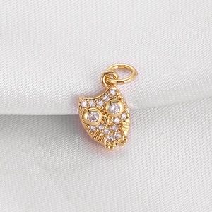 Macro view of a gold-plated owl pendant with pink cubic zirconia on white silk
