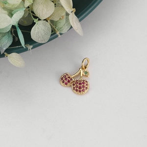Detailed close-up of cherry charm with red cubic zirconia and green leaf in gold setting