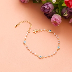 Detail of gold evil eye bracelet with white beads and lobster clasp on peach background