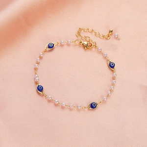 Detail of gold evil eye bracelet with white pearls on a pink satin fabric background