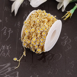 Golden DIY chain with white enamel daisy charms wound on a spool for jewelry making
