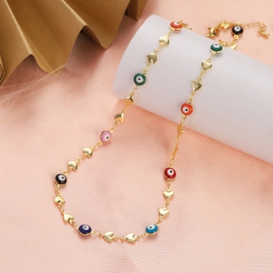 Detail of gold heart chain necklace featuring colorful evil eye charms on a pink fabric background