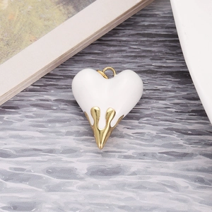 Macro detail of white enamel heart pendant with gold dripping metal accents and top ring