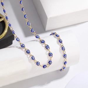 Gold stainless steel evil eye necklace displayed on a white cylindrical pedestal