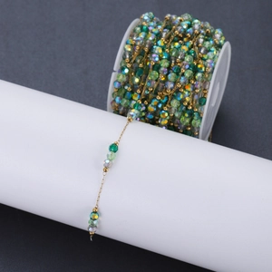 DIY jewelry chain with green crystal beads and gold metal links on a white spool