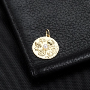 Macro detail of 14K gold plated pendant with embossed starfish and pearl on leather