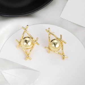 Artistic golden metal ball earrings with crisscross geometric frame on white stand