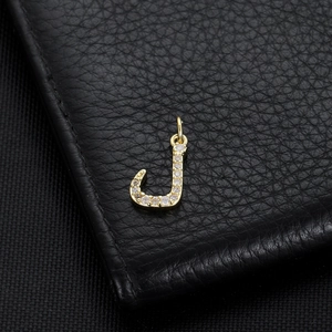 Macro shot of 14K gold plated letter J pendant with white zircons on black leather