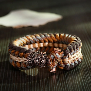 Dettaglio bracciale paracord con fibbia drago in bronzo antico su legno rustico