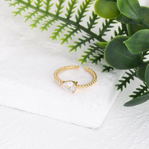 Detalle de anillo dorado trenzado con circonita en forma de pera y textura de cuentas