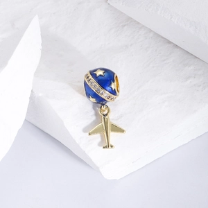 Makroaufnahme: Blauer Emaille-Planet mit goldenen Sternen, Ring und Flugzeug-Anhänger