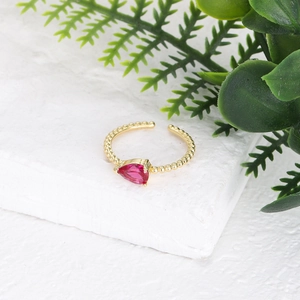 Detalle de anillo dorado trenzado con circón rojo pera y textura de cuentas elegante