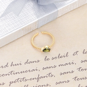 Primer plano de anillo dorado trenzado con gema verde en forma de pera y textura de cuentas