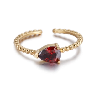 Detalle de anillo trenzado dorado con circón rojo en forma de pera engastado en garras