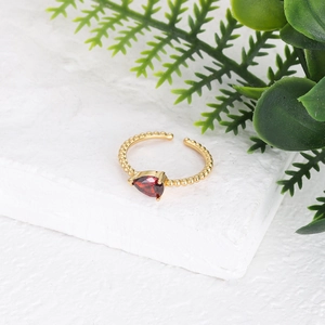 Detalle de piedra roja de pera en anillo ajustable dorado con textura de cuentas