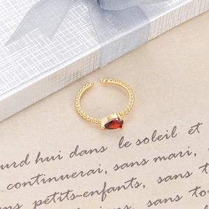 Detalle de un anillo de cuentas doradas con gema roja en forma de pera sobre una caja