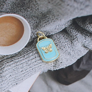 Detailed view of rectangle light blue enamel pendant with gold butterfly relief and hanging ring