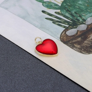 Detail van een rode emaille hartvormige hanger met gouden rand voor sieraden maken