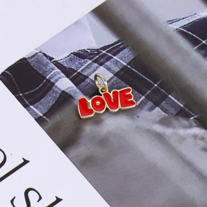 Close-up of red enamel and 14K gold plated LOVE pendant charm on a stylized background
