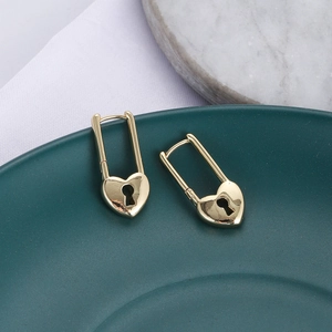Dettaglio di orecchini huggie a lucchetto a cuore oro su un piatto di ceramica verde