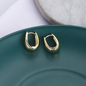 Dettaglio di orecchini a cerchio in zircone dorato a forma di U su un vassoio verde scuro