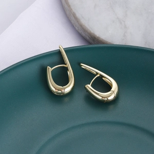 Orecchini geometrici a forma di U in oro lucido su un vassoio di ceramica scura