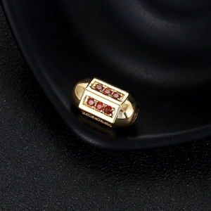 Détail macro d'une perle capsule dorée sertie de zircons rouges sur fond texturé noir