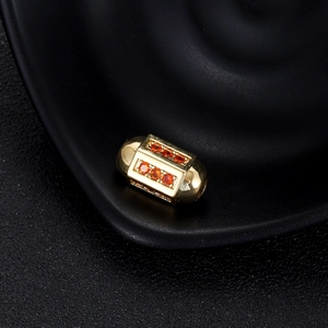 Vue macro d'une perle barillet dorée avec zircone orange sur un plateau noir texturé
