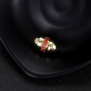 Gros plan sur une perle cylindrique dorée avec zircon orange et texture rainurée
