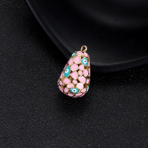 Détail du pendentif goutte doré avec cœur en émail rose et charme œil protecteur