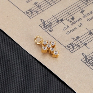 Close-up of golden geometric H-shaped pendant with six clear zircon stones on sheet music