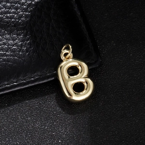 Macro shot of 3D gold bubble letter B pendant with a polished mirror finish on black leather