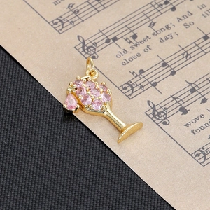 Detail showing a golden wine glass pendant set with sparkling pink gemstones and a ring