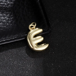 Macro detail of glossy golden 3D balloon letter E pendant on black leather background