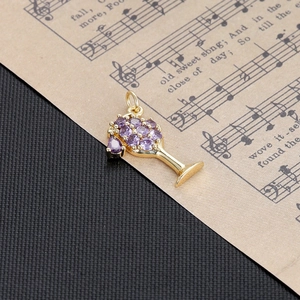 Detailed view of a gold wine glass pendant set with purple crystals on a vintage music sheet