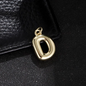Detailed macro view of a polished gold letter D balloon pendant on black leather