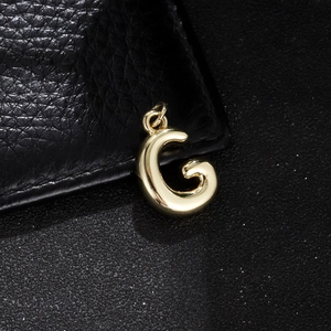 Detailed close-up of a 3D bubble letter G pendant in polished gold on a black texture