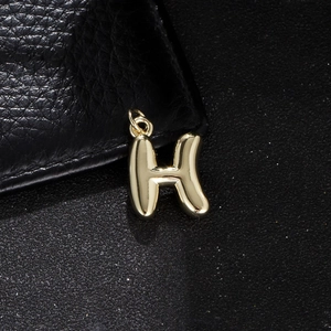 Macro shot of a golden bubble letter H charm with a polished mirror finish on black leather