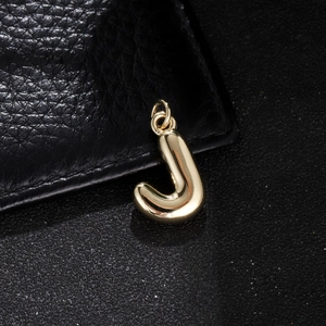 Macro shot of bubble letter J pendant with shiny gold finish on black leather background