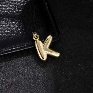 Macro view of gold balloon letter K pendant with polished mirror finish and ring bail