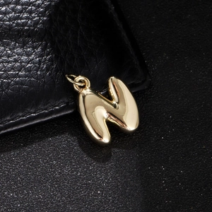 Macro detail of golden 3D bubble letter N pendant with high-shine mirrored finish