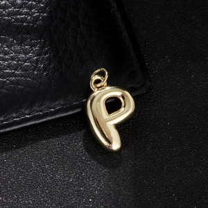 Macro shot of polished gold bubble letter P pendant on black textured leather surface
