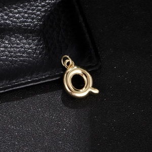 Macro shot of polished gold bubble letter Q pendant on black leather textured surface