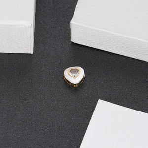 Detail of heart-shaped copper bead with white enamel finish and inset zircon stone